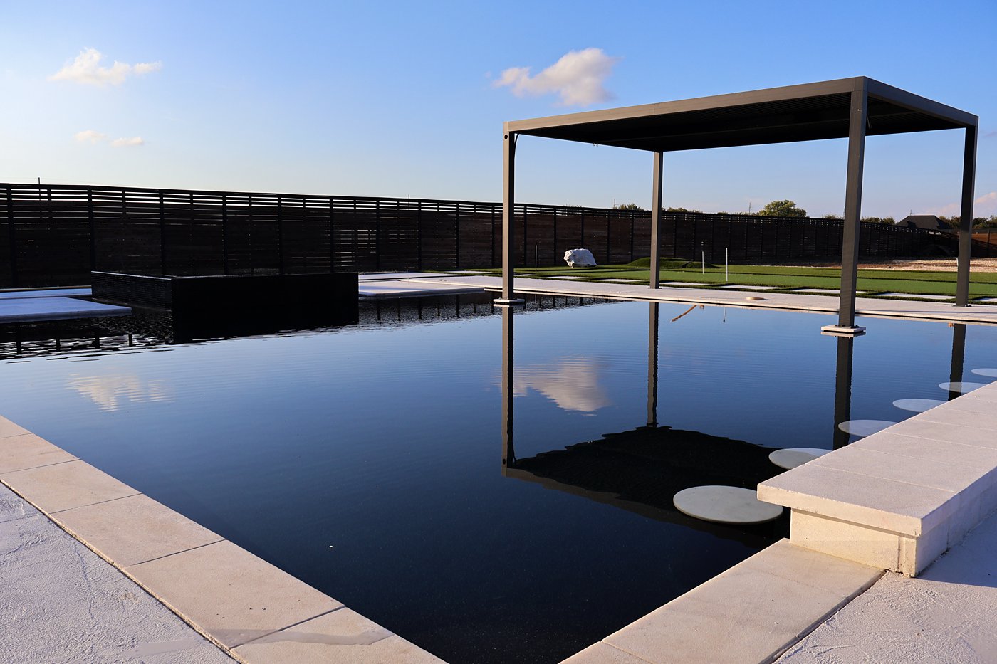 Black mirror-finish pool with a modern pergola and stepping pads