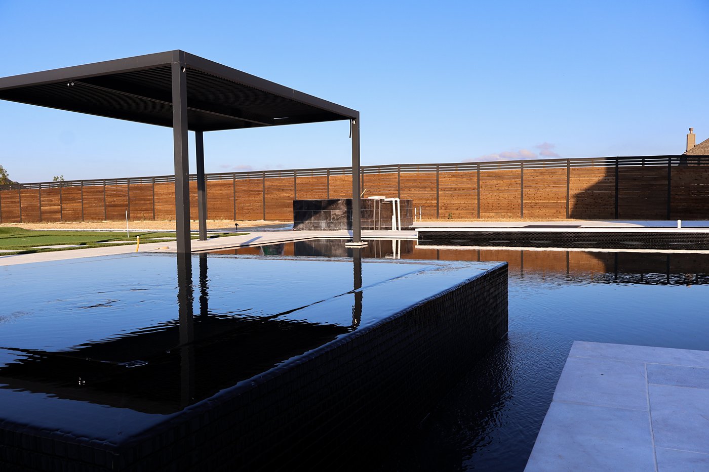Raised black-tile spa with a pergola and mirror-finish pool